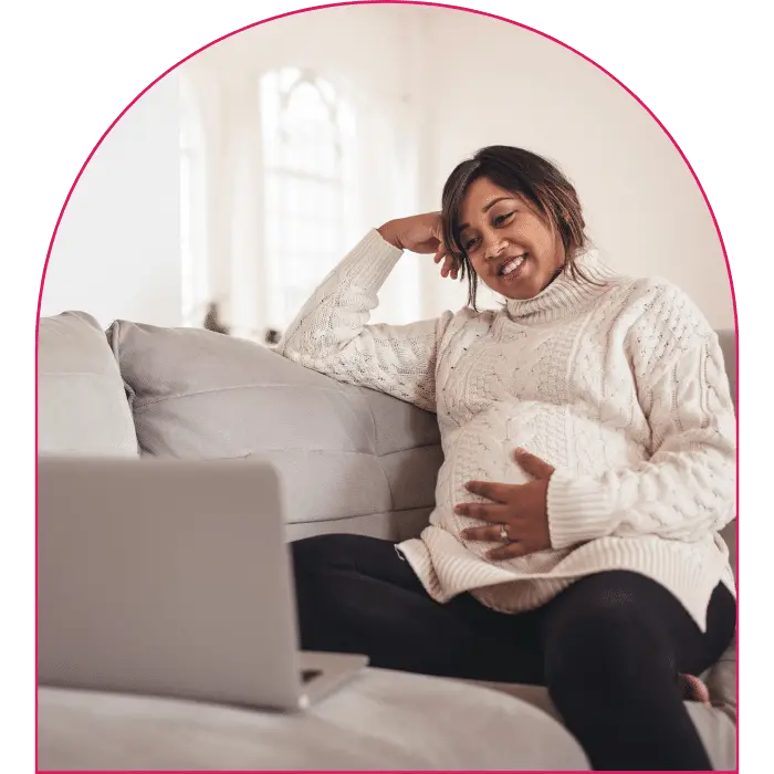 Femme Pharm Range: Happy pregnant woman sitting on couch looking at laptop