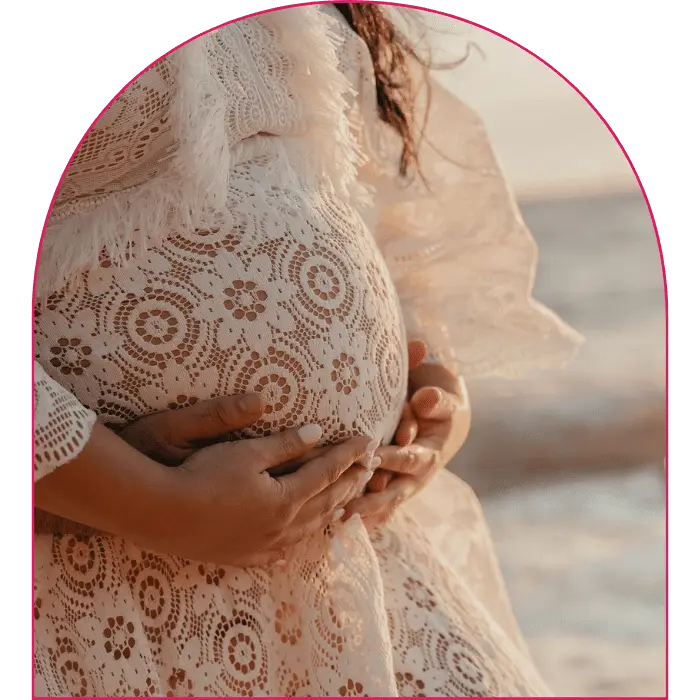 Close up of pregnant woman's belly wearing in a white dress, with two sets of hands holding baby bump