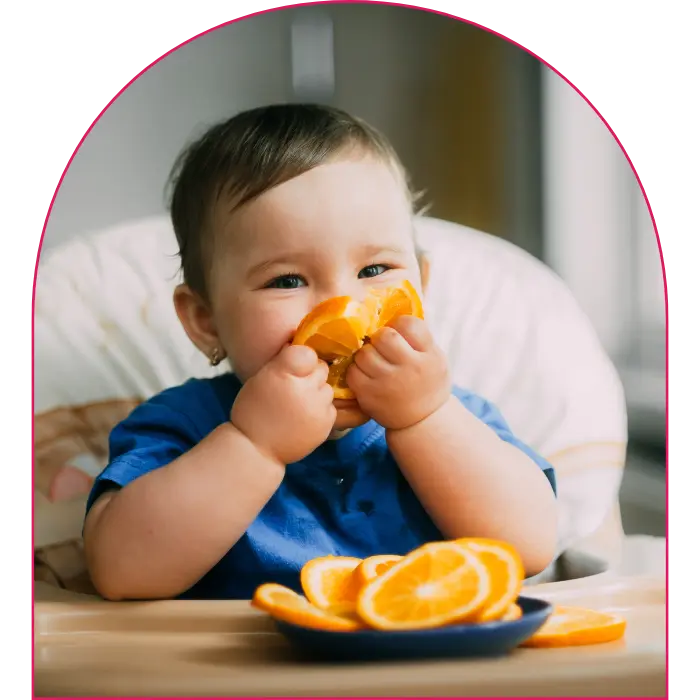 Little baby sitting in high chair eating an orange